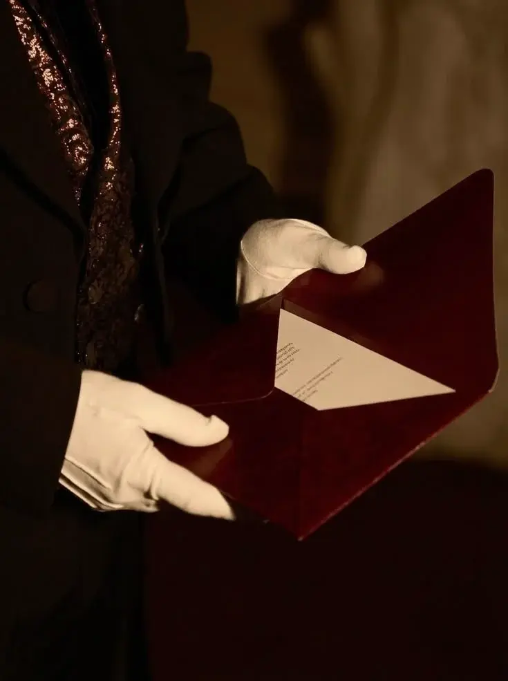 Close-up shot of a butler in white gloves opening a dark red envelope with a formal letter inside representing e mail marketing.